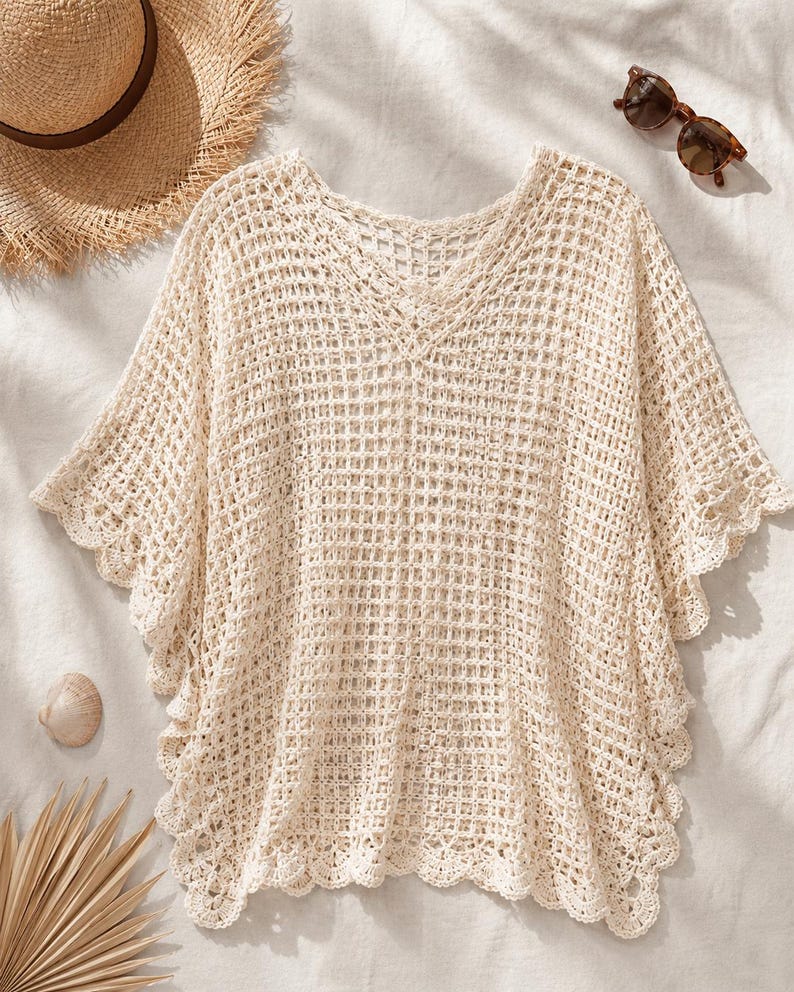May include: A cream-colored crochet top featuring a V-neckline, short wide sleeves, and a grid-like openwork pattern. The garment is finished with a scalloped edge along the sleeves and hemline, providing a textured and lightweight appearance.