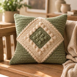 May include: A square crochet pillow cover in sage green featuring a central cream-colored diamond motif. The design includes a textured border of small bobble stitches surrounding the diamond, with a matching bobble stitch pattern in the center.