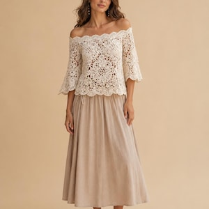 Könnte beinhalten: Off-White Häkeltop mit schulterfreiem Design, Dreiviertelärmeln und einem wellenförmigen Ausschnitt. Kombiniert mit einem langen, beigefarbenen Rock und Sandalen. Der Look ist im Boho-Stil gehalten.