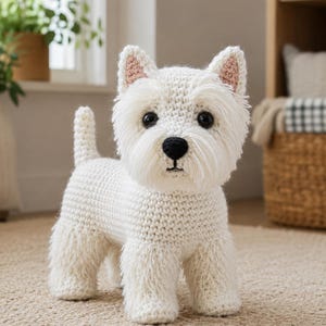 Puede incluir: Un perro de peluche tejido a ganchillo en color blanco, tipo Westie, con cuerpo de hilo texturizado, nariz negra, ojos redondos oscuros y orejas pequeñas con forro rosa. El perro de peluche está de pie con una cola corta y pelo desgreñado.