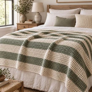 Könnte beinhalten: Eine rechteckige Häkeldecke mit abwechselnden horizontalen Streifen in Creme und Salbeigrün. Das Textil weist ein durchgehendes, strukturiertes Muster mit offenen Maschen auf und liegt flächig auf einem Bett, was ihm ein weiches Aussehen verleiht.