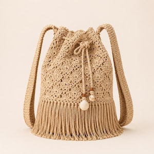 May include: A beige crochet drawstring backpack with long shoulder straps and a fringe bottom. The bag features a detailed floral pattern and is adorned with a seashell and wooden bead accents. The bag is perfect for carrying beach essentials.
