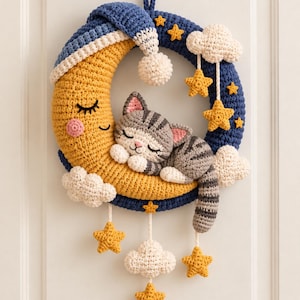Peut inclure: Une décoration murale circulaire en crochet représentant un croissant de lune jaune au visage endormi, coiffé d'un bonnet de nuit bleu. Un chat tigré gris dort sur la lune, entouré de nuages blancs et d'étoiles jaunes suspendus à l'anneau bleu.