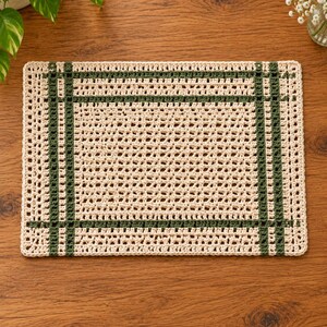 Op de afbeelding: Een rechthoekige gehaakte placemat met een cr&egrave;mekleurige basis en een rasterachtig patroon van donker bosgroen garen. Het ontwerp bestaat uit een centraal gedeelte met open steken, omlijst door dubbele verticale en horizontale groene strepen.