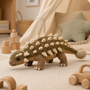 Op de afbeelding: Een gehaakt ankylosaurus-speeltje met een donker olijfgroen lichaam en lichtbeige stekels langs de rug en staart. De dinosaurus heeft een ronde kop met donkere veiligheidsogen, vier stevige poten en een staart met een knotsvormig uiteinde.