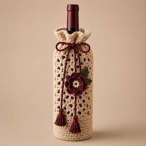 May include: A beige crochet bottle cover featuring a lattice pattern, a drawstring closure with dark red tassels, and a decorative dark red flower applique with a green leaf. The cover is placed over a dark red wine bottle neck.