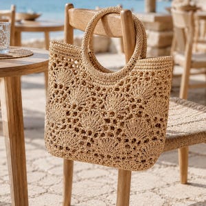 Pode incluir: Uma bolsa tote bege feita de material de palha trançada, apresentando um padrão detalhado de conchas vazadas em todo o corpo e duas alças circulares integradas no topo. A bolsa possui um formato retangular estruturado com base plana.