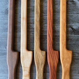 May include: Five vertical wooden door handles arranged side by side, each featuring a distinct wood grain and color ranging from dark brown to light tan. Each handle has a long, straight body with a curved top hook and a wider, rounded base.