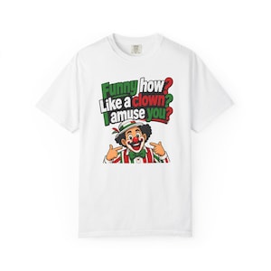 May include: A white short-sleeve t-shirt featuring a graphic of a clown wearing a striped shirt and green bow tie. The text above the clown reads, "Funny how like a clown I amuse you?" with "Funny" in green, "clown" in red, and question marks in red and green.