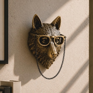 May include: A bronze-toned wall-mounted sculpture of a fox head featuring detailed fur texture. The fox is wearing a pair of matching bronze-coloured glasses with a thin metal chain hanging down from the frames, creating a decorative display piece.