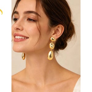 Könnte beinhalten: Goldfarbene Ohrhänger mit drei Steinen. Die Ohrringe haben eine polierte, organische Form mit einem großen, tropfenförmigen Stein unten. Der Text "Luvera Jewelry" ist sichtbar.