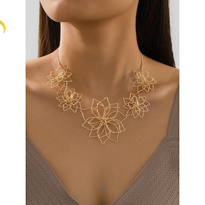 Könnte beinhalten: Eine goldfarbene Halskette mit floralem Design. Die Halskette hat mehrere Anhänger in Form von durchbrochenen Blumen unterschiedlicher Größe, die durch filigrane Ketten verbunden sind. Die Halskette wird um den Hals getragen. Der Text "Luvera Jewelry" befindet sich in der oberen linken Ecke.