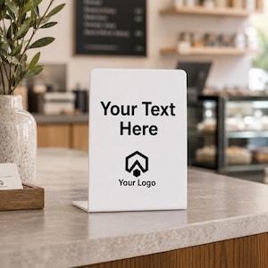 May include: A white, L-shaped acrylic sign holder featuring the black printed text Your Text Here and a black geometric logo above the words Your Logo. The sign is positioned upright on a flat surface, providing a clear display for custom signage.