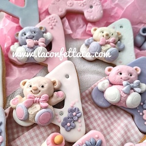 Puede incluir: Una colección de galletas con forma de número cuatro decoradas con ositos de fondant en tonos pastel, pequeñas flores y pedrería. Las galletas presentan varios tonos de rosa, azul y blanco, con el texto www.laconfettata.com visible.