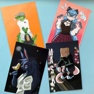 May include: Four rectangular art prints featuring illustrated characters. One shows a green crocodile in a white shirt, another a blue-haired character with the text Nya, one a dark-furred creature with a flower, and one a figure with a paper bag mask labelled Mask.