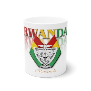 Può includere: Una tazza in ceramica bianca con la parola RWANDA in grandi lettere colorate nella parte superiore. Al centro è raffigurato lo stemma del Ruanda, con uno scudo recante il testo RÉPUBLIQUE RWANDAISE e LIBERTÉ-COOPÉRATION-PROGRÈS. La parola Rwanda è stampata in corsivo dorato in basso.