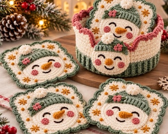 May include: A set of four square crochet coasters featuring a smiling snowman face with a green hat, pink cheeks, and an orange nose, accompanied by a matching round crochet basket with a scalloped edge and a snowman face on the front.