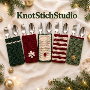 May include: Five rectangular crochet cutlery holders labeled KnotStichStudio. Each holds a silver fork, knife, and spoon. Designs include solid dark green, red with a white snowflake, cream with a red button, red and white stripes, and olive green with a gold star.