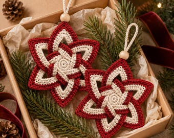 May include: Two star-shaped crochet ornaments featuring an intricate interwoven pattern in deep red and cream yarn. Each ornament is topped with a natural wooden bead and a cream-colored cord loop for hanging, presented in a cardboard box.