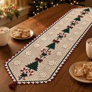 Puede incluir: Un camino de mesa de ganchillo largo y rectangular en color crema, con un patrón repetitivo de árboles de Navidad verde oscuro, lazos rojos y bastones de caramelo. El camino tiene un borde festoneado rojo y blanco con pequeñas borlas.