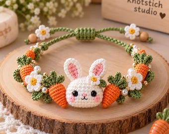 May include: A crochet bracelet featuring a central white bunny head with pink inner ears, flanked by orange carrots with green tops and small white flowers with yellow centers. The band is made of green braided cord with adjustable sliding knots.