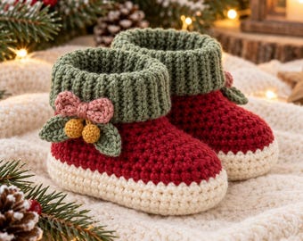 May include: A pair of handmade crochet booties featuring a deep red body, a cream-colored sole, and a ribbed olive green cuff. Each bootie is decorated with a small pink bow and two yellow berries attached to green leaves.