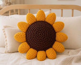May include: A round, crocheted sunflower pillow featuring a dark brown circular center and bright yellow petals radiating outward. The textured yarn construction creates a distinct floral shape with a soft, plush appearance for the decorative cushion.