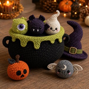 May include: A black crochet cauldron with a green dripping rim, containing a green cyclops, a purple bat, and a white ghost. Beside it sits a purple witch hat, an orange pumpkin with a black face, and a gray moth with a crescent moon symbol.