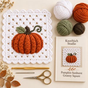 Könnte beinhalten: Ein weißes gehäkeltes Granny Square mit einem strukturierten orangefarbenen Kürbis, einem grünen Blatt und einer Ranke, dazu Knäuel aus weißem, orangefarbenem, grünem und braunem Garn, eine goldene 5,0-mm-Häkelnadel, eine Nadel, eine Schere und ein Buch.