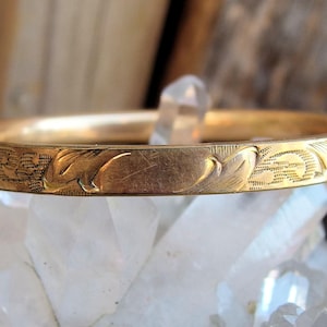 May include: A gold bangle bracelet with an intricate floral design. The bracelet is thin and delicate, and it has a polished finish.