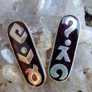 Peut inclure: Deux pendentifs en argent avec émail noir. Un pendentif présente un point d'interrogation et une figure stylisée, l'autre présente un motif géométrique.