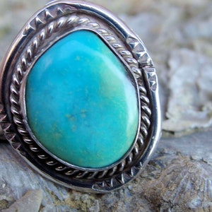 Könnte beinhalten: Ein silberner Ring mit einem Türkis-Stein, der in einem Seil-Design gefasst ist. Der Stein ist hellblau mit grünen und braunen Adern.