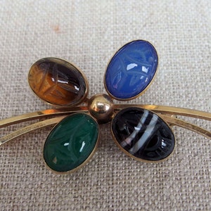 May include: A gold tone brooch with five oval shaped stones. The stones are carved with an Egyptian scarab beetle design. The stones are blue, green, brown, black and white.