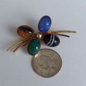 May include: A gold tone pin with four carved gemstone cabochons. The stones are blue, green, brown, and black and white.