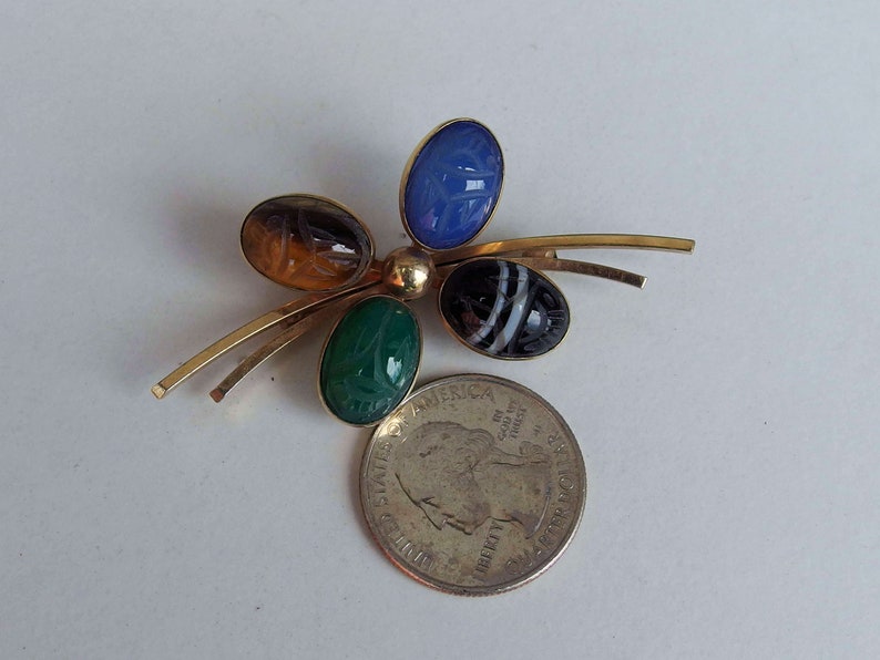 May include: A gold tone pin with four carved gemstone cabochons. The stones are blue, green, brown, and black and white.