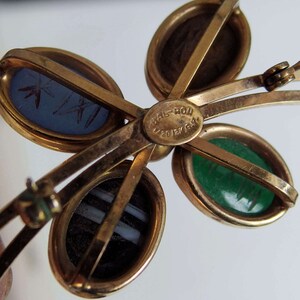 May include: Gold tone brooch with four oval shaped cabochons. The cabochons are blue, green, brown, and white. The brooch has a hinged clasp and is marked "Val-Ron Jewelry".