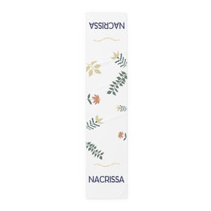May include: A white rectangular table runner featuring a repeating botanical pattern of dark green leaves, light yellow leaves, and small orange flowers. The text NACRISSA is printed in dark blue at both ends, with small yellow text between the motifs.