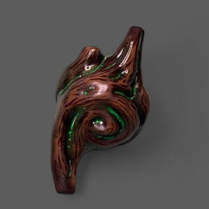 Puede incluir: Una ocarina de cerámica marrón brillante con forma de trozo de madera o raíz retorcida. La superficie presenta texturas de veta de madera de color marrón oscuro con acentos de pintura verde brillante en las grietas y espirales.