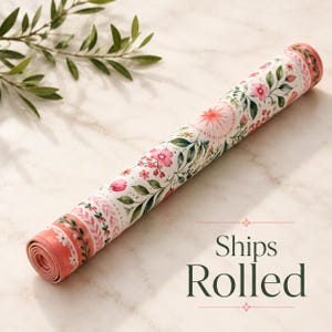 May include: A cylindrical mat rolled tightly, featuring a white background with a repeating pattern of pink flowers, green leaves, and small starburst motifs. The edges of the mat display a decorative border with pink and green botanical elements.