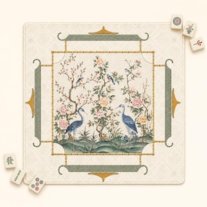 May include: A square mahjong mat featuring a central illustration of two blue cranes standing among flowering trees and smaller birds. The border is framed by a bamboo-style pattern and green decorative panels. Several mahjong tiles are scattered.