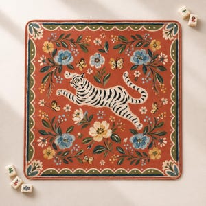 May include: A square mat with a rust-orange background featuring a central white tiger with black stripes in a leaping pose. The design includes blue and yellow flowers, green leaves, and small butterflies, all framed by a scalloped green border.