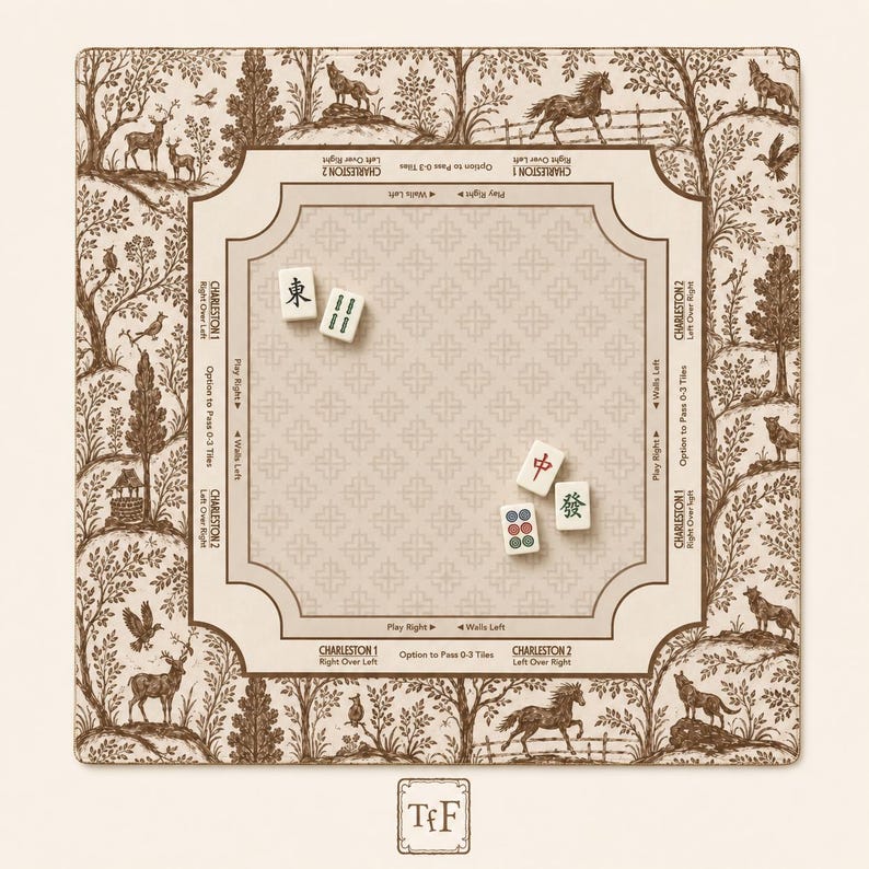 May include: A square Mahjong mat featuring a cream-colored center with a repeating cross pattern and brown border text detailing Charleston rules. The outer edge displays a brown and cream toile-style forest scene with animals. Four Mahjong tiles are placed on the mat.