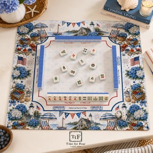 K&ouml;nnte beinhalten: Eine quadratische Mahjong-Matte mit K&uuml;stenmotiv, Leuchtt&uuml;rmen, blauen Hortensien, Strandst&uuml;hlen und amerikanischen Flaggen. Die Matte enth&auml;lt aufgedruckte Spielanleitungen, Charleston-Passregeln sowie einen Bereich mit Spielsteinen.
