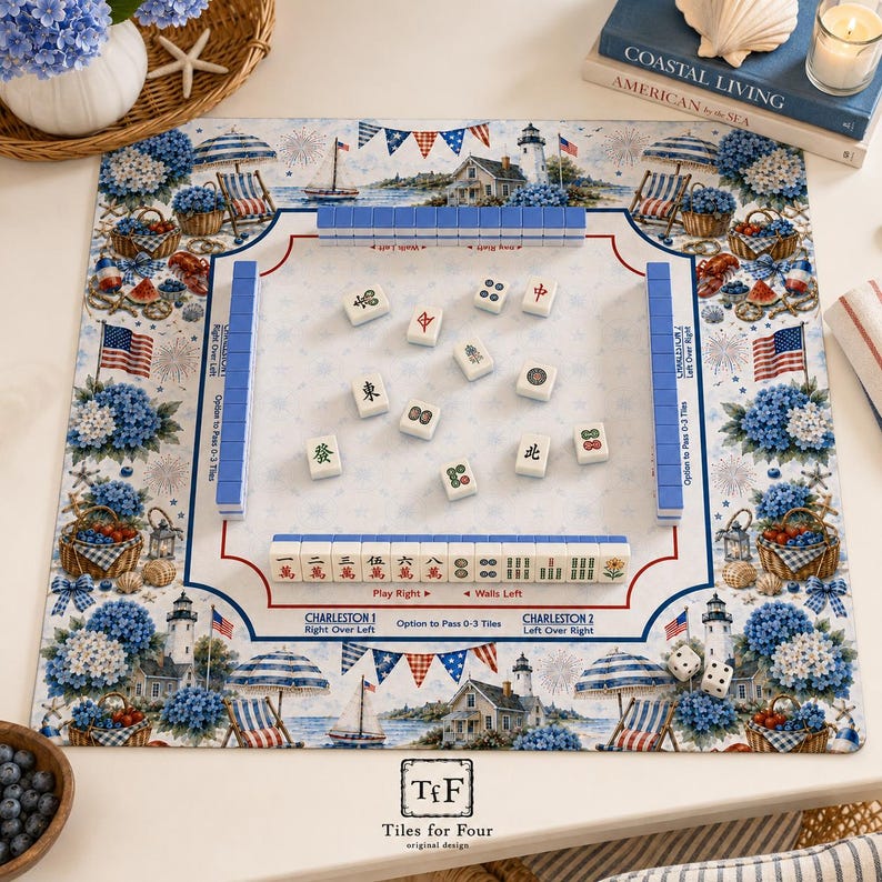 K&ouml;nnte beinhalten: Eine quadratische Mahjong-Matte mit K&uuml;stenmotiv, Leuchtt&uuml;rmen, blauen Hortensien, Strandst&uuml;hlen und amerikanischen Flaggen. Die Matte enth&auml;lt aufgedruckte Spielanleitungen, Charleston-Passregeln sowie einen Bereich mit Spielsteinen.