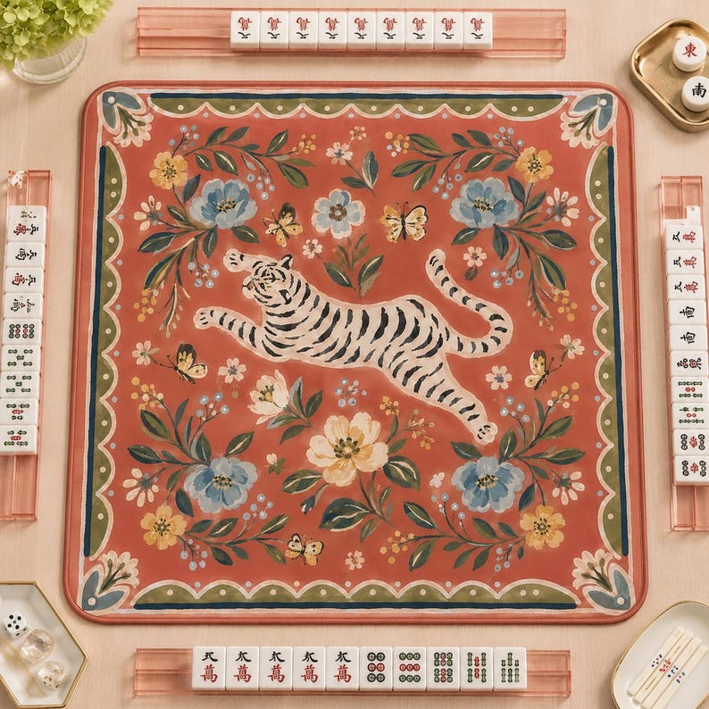 May include: A square mahjong mat featuring a central leaping tiger surrounded by blue and yellow floral patterns on a terracotta background. The mat is bordered by a scalloped green edge and is surrounded by four acrylic tile racks and tiles.