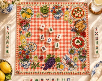 May include: A square game board featuring a red and white checkered pattern with illustrations of lemons, grapes, flowers, pizza, and bread, surrounded by four clear racks holding white mahjong tiles with red, green, and blue Chinese characters.