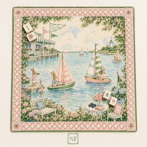 May include: A square decorative fabric mat featuring a watercolor illustration of rabbits sailing on a lake near a clubhouse. The border has a pink lattice pattern with green edges. Two mahjong tiles are placed on the mat, one with red text.