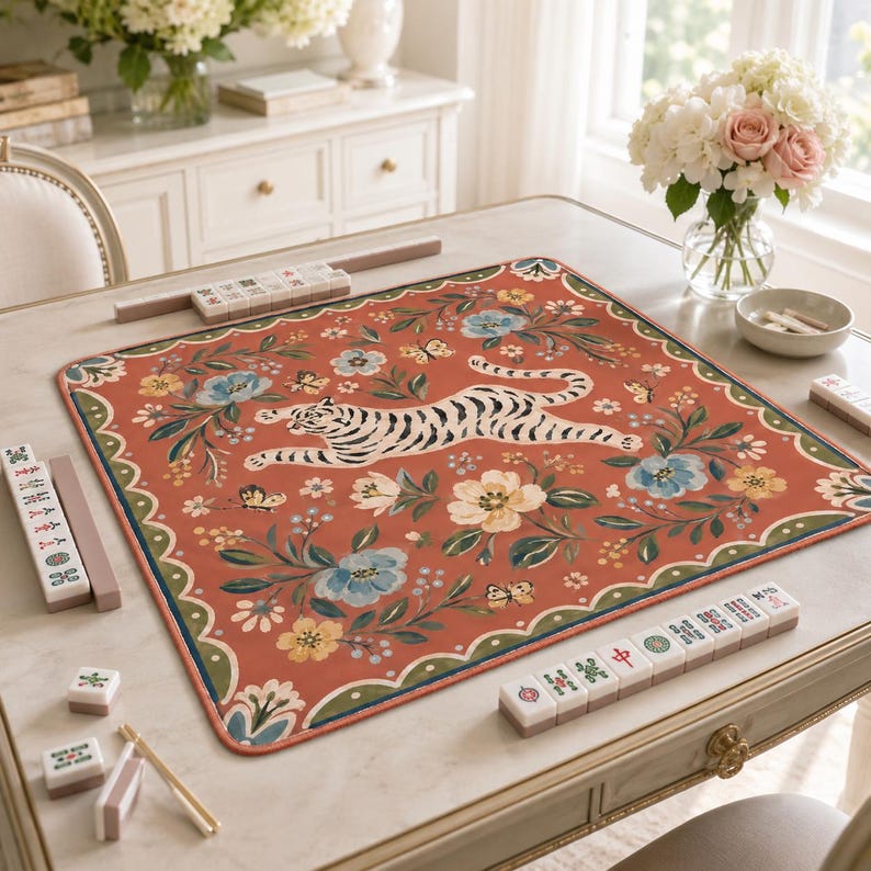 May include: A rectangular mahjong mat with a terracotta orange background featuring a central white tiger with black stripes, surrounded by a floral pattern of blue and yellow flowers, green leaves, and small butterflies, with mahjong tiles.