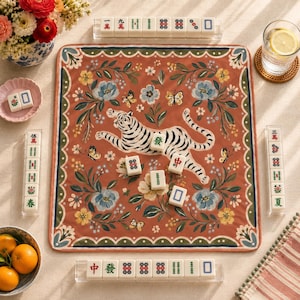 May include: A square mahjong mat featuring a terracotta background with a central white tiger illustration, surrounded by blue and yellow floral patterns and butterflies. The mat is bordered by green and white scalloped edges, with mahjong tiles.
