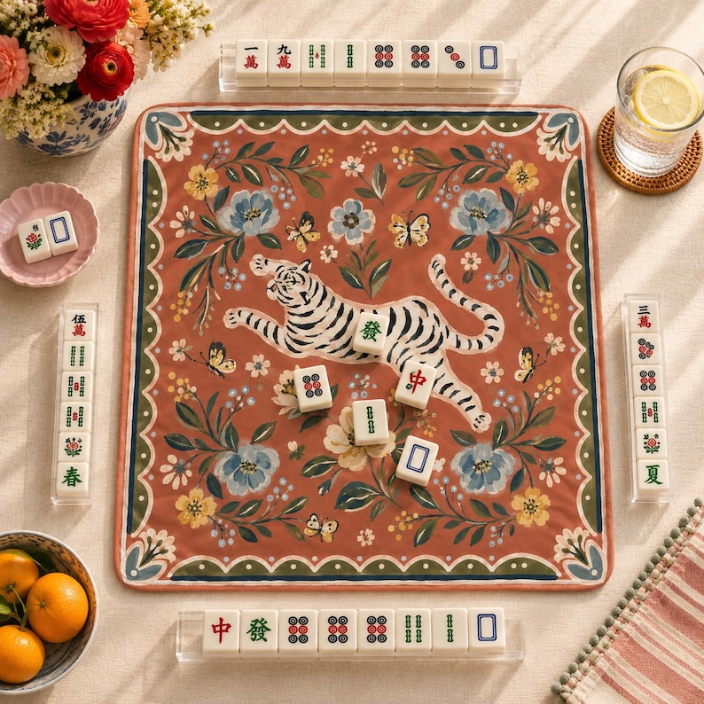 May include: A square mahjong mat featuring a terracotta background with a central white tiger illustration, surrounded by blue and yellow floral patterns and butterflies. The mat is bordered by green and white scalloped edges, with mahjong tiles.